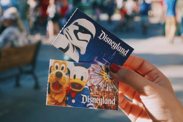 Two Disneyland tickets are being held up, one featuring a stormtrooper and the other showcasing Goofy, Donald Duck, and a Ferris wheel.