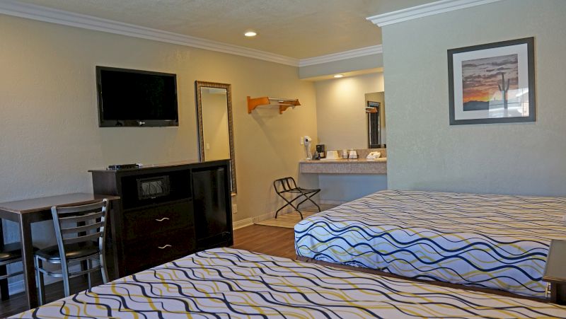 A hotel room with two beds, a TV, a desk, and a kitchenette.