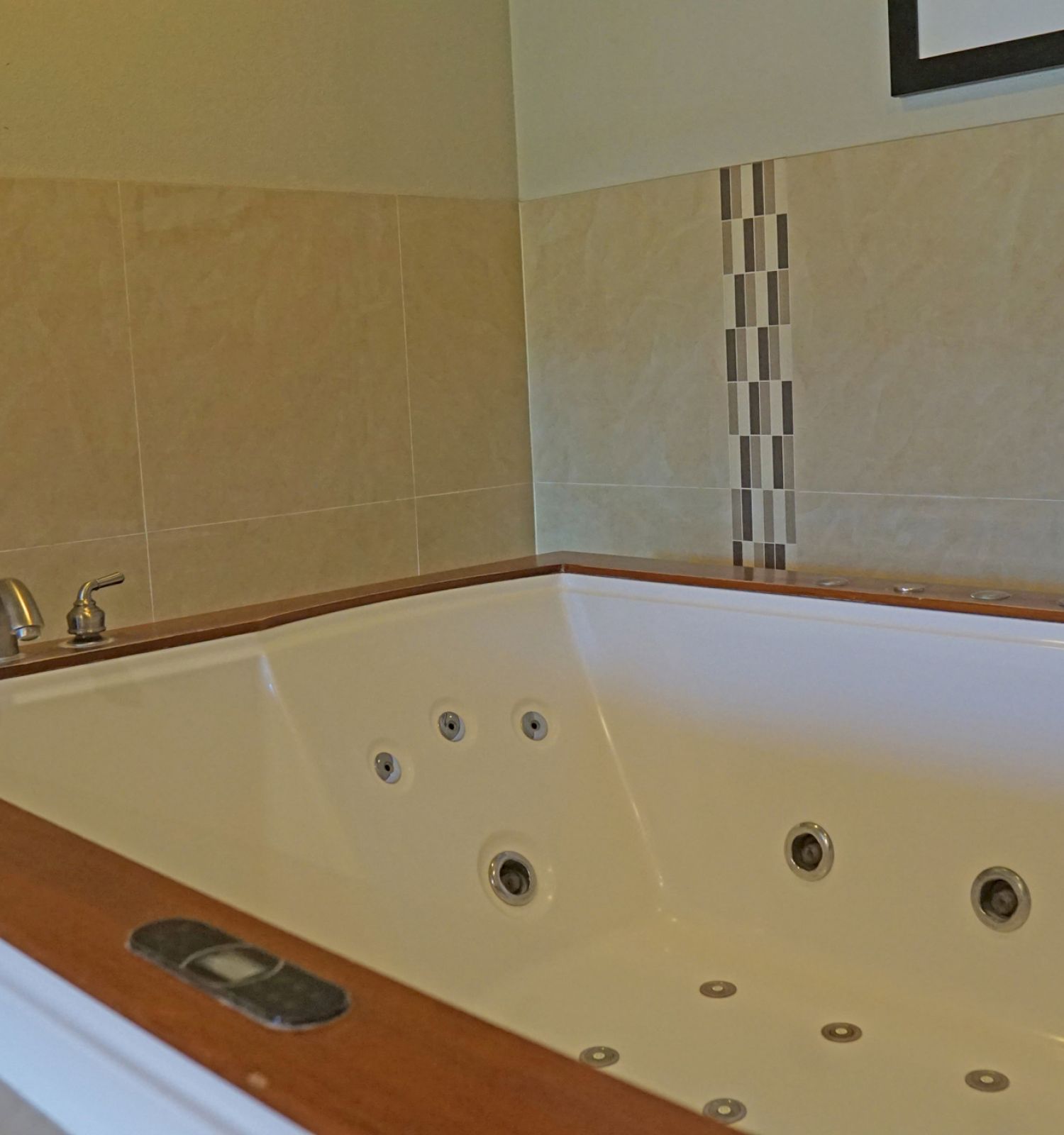 This image shows a corner of a bathroom with a white whirlpool bathtub, featuring multiple jets, tan tiles, a folded white towel and a silver faucet.