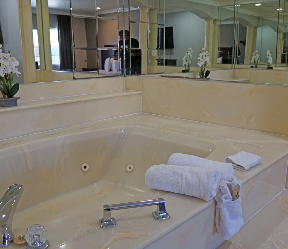 A large jacuzzi tub with a silver faucet and handles, and a stack of white towels beside it.