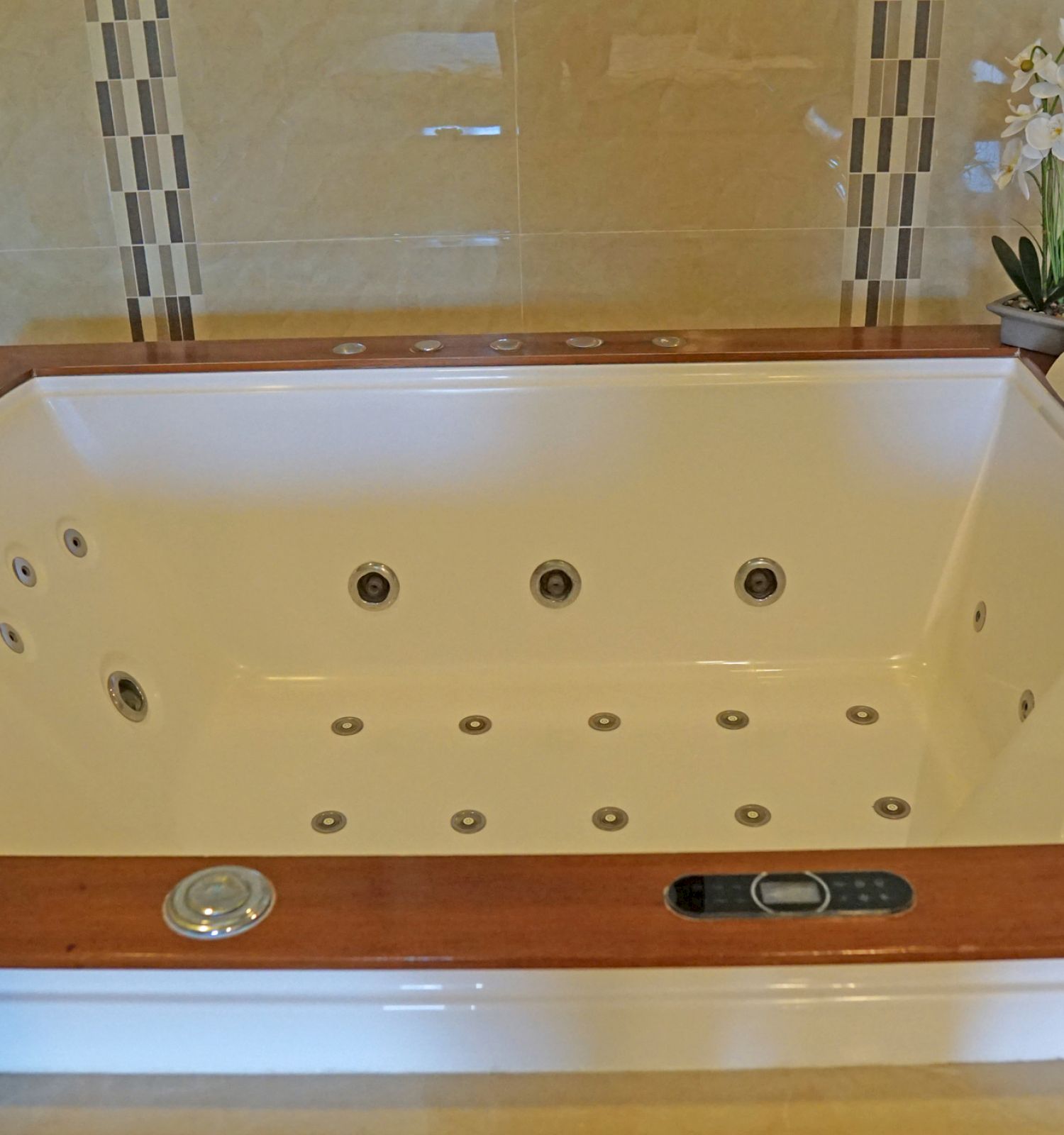 An image of a luxurious, white jacuzzi bathtub with wooden trim, equipped with multiple jets and controls, and decorated with flowers and towels.