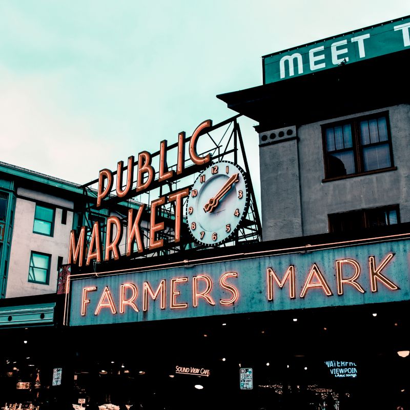 This image shows a famous building with the signs "Public Market" and "Farmers Market" prominently displayed, lights glowing, and a clock centered above.