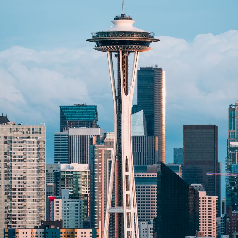The image shows the Space Needle in Seattle, Washington, with city skyscrapers in the background under a blue sky.