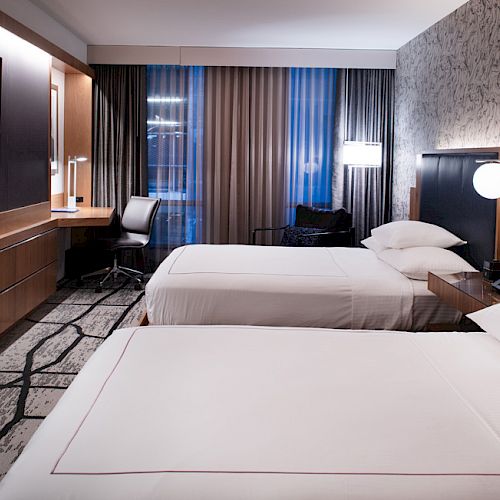 A modern hotel room features two neatly made beds, a wall-mounted TV, a workdesk with a chair, and contemporary decor ending the sentence.