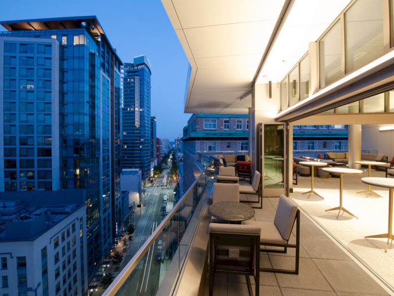 A balcony with seating area overlooking a city skyline at dusk.
