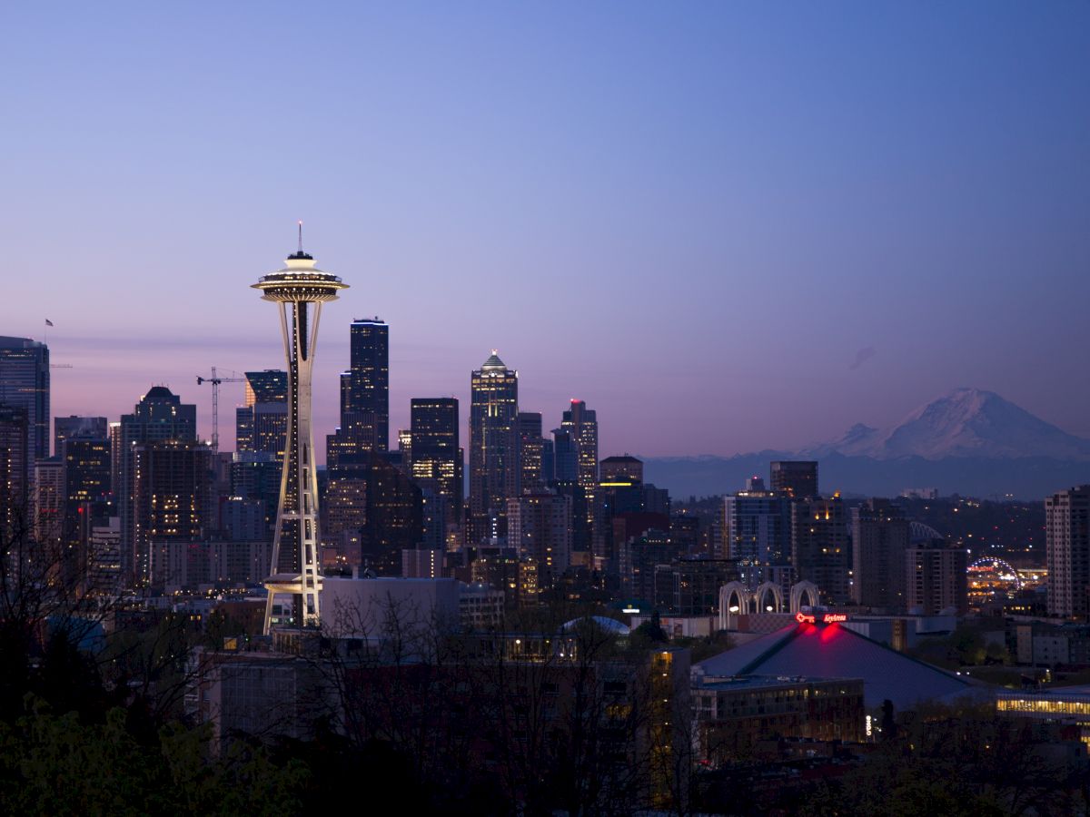 This image shows the Seattle skyline at dusk, featuring the Space Needle and surrounding buildings, with Mount Rainier visible in the background.