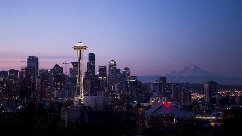 This image shows the Seattle skyline at dusk, featuring the Space Needle and surrounding buildings, with Mount Rainier visible in the background.