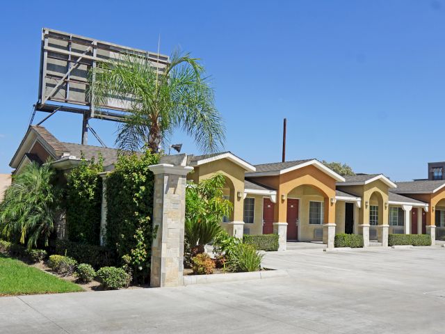 A photo of a motel exterior with a driveway and palm trees.