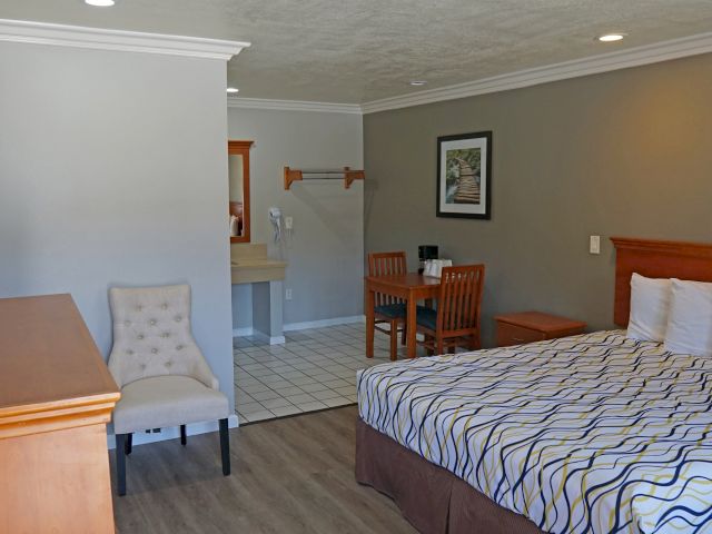 A wide view of a hotel room with a bed, desk, chair, and nightstand.