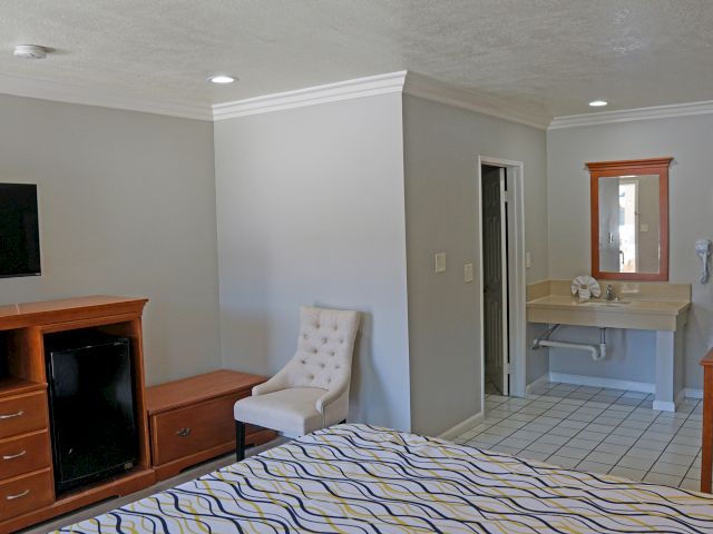 A wide view of a hotel room with a bed, TV, chair, and bathroom sink.