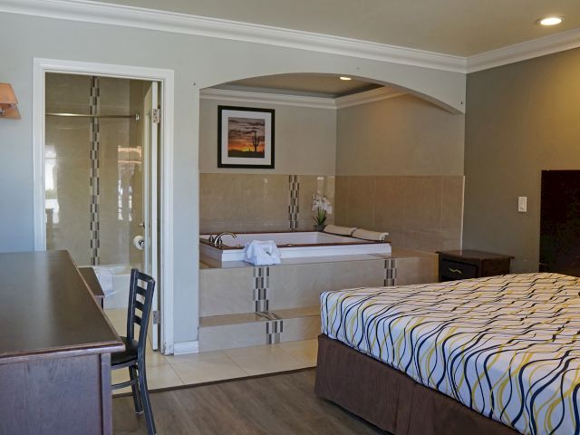 A hotel room with a bed, a desk, a chair, a large tub in an alcove, and a shower in the background.