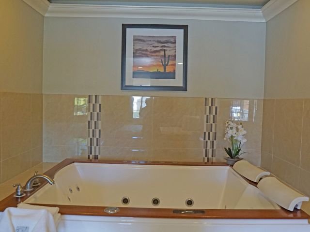 A large jacuzzi tub with wooden trim and tiled walls, adorned with a flower vase and towels.