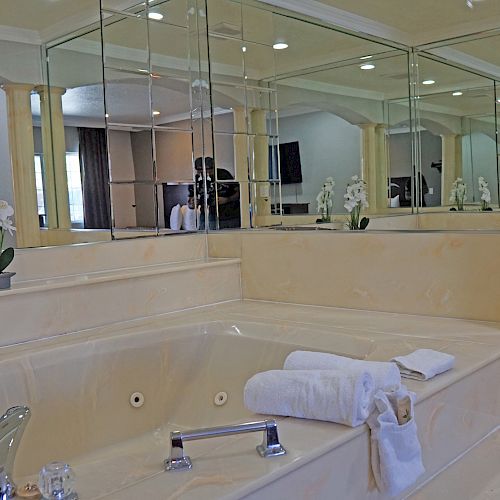 The image depicts a luxurious bathroom with a large bathtub, mirrors, and rolled towels, along with a potted orchid placed on the bathtub edge.