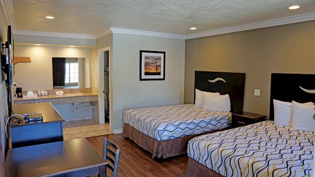 A hotel room with two beds, a desk, and a bathroom in the background.