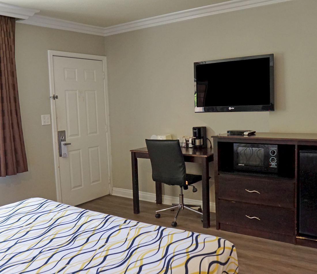 A hotel room with a bed, desk, TV, and microwave