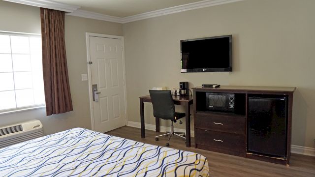 A hotel room with a bed, desk, TV, and mini-fridge.