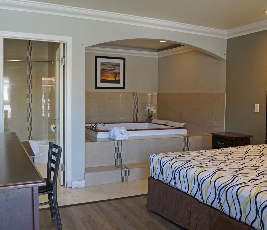 A hotel room with a large bed, desk, chair, and a jacuzzi tub in the bathroom