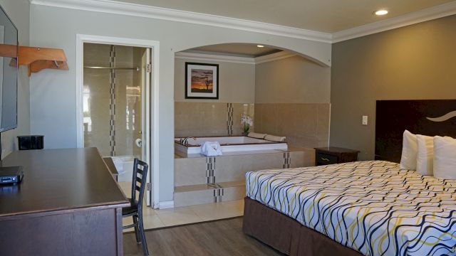 A wide view of a hotel room with a king-sized bed, desk, and a separate jacuzzi tub in the bathroom area.