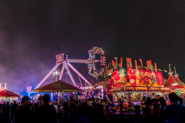 A lively amusement park at night with colorful rides, booths, and crowds of people enjoying the attractions.