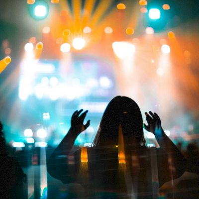 People are enjoying a concert with vibrant stage lights creating a lively atmosphere, and silhouettes of the audience are visible.